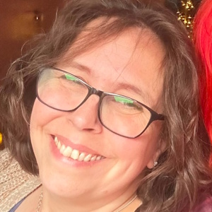 A white woman with glasses and bobbed wavy brown hair smiles at the camera