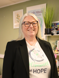 Our Founder Aine Wallace, wearing a blazer and a Fresh Minds Education in white with the word 'hope' visible, is smiling at the camera.