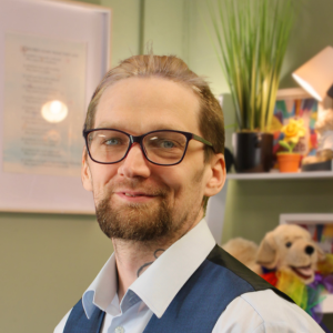 A white person with glasses and a beard smiles at the camera