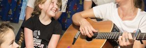 A group of children and a Bamber Bear with an adult playing guitar, they are smiling and singing